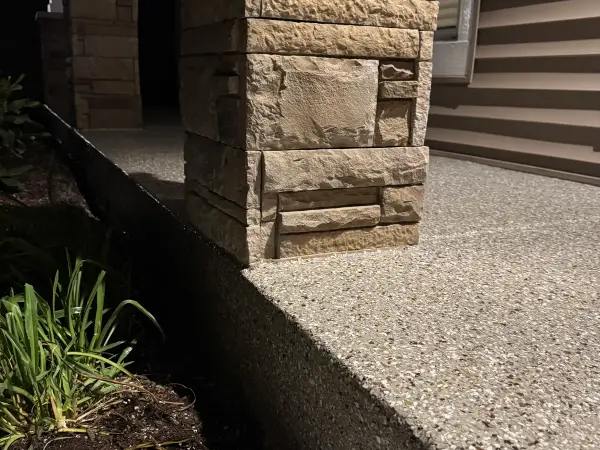 Porch step edge finished with polyurea flake coating beside a stone pillar