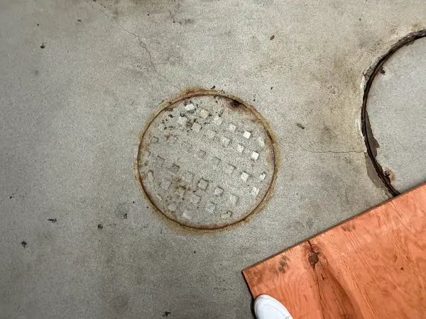 Rusted floor plate and cracked concrete around utility covers before coating