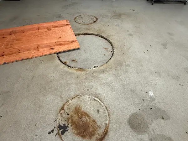 Stained garage floor with rusty access covers and oil spots before prep