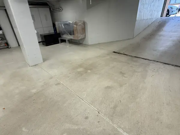 Worn bare concrete garage floor and ramp with tire marks before coating
