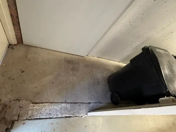 Dirty concrete floor beside garage door with crumbling edge near threshold