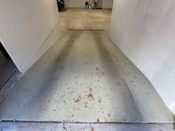 Garage entrance ramp with tire tracks, debris and worn concrete before coating