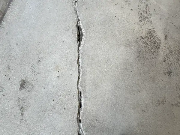 Wide crack in bare concrete garage floor before repair