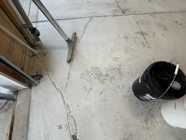 Branching cracks near garage door opening on stained bare concrete