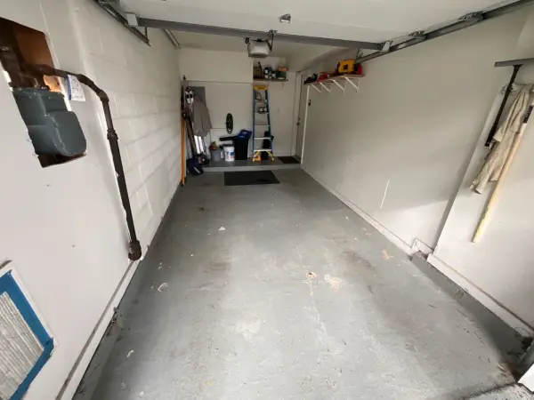 Single-car garage floor before coating with worn gray paint and debris